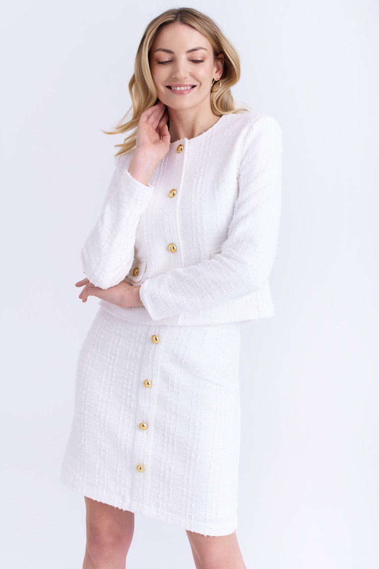 Woman wearing a white textured tweed jacket and matching mini skirt with gold buttons